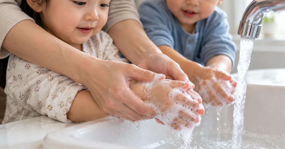 Người lớn hướng dẫn trẻ rửa tay bằng xà phòng dưới vòi nước sạch